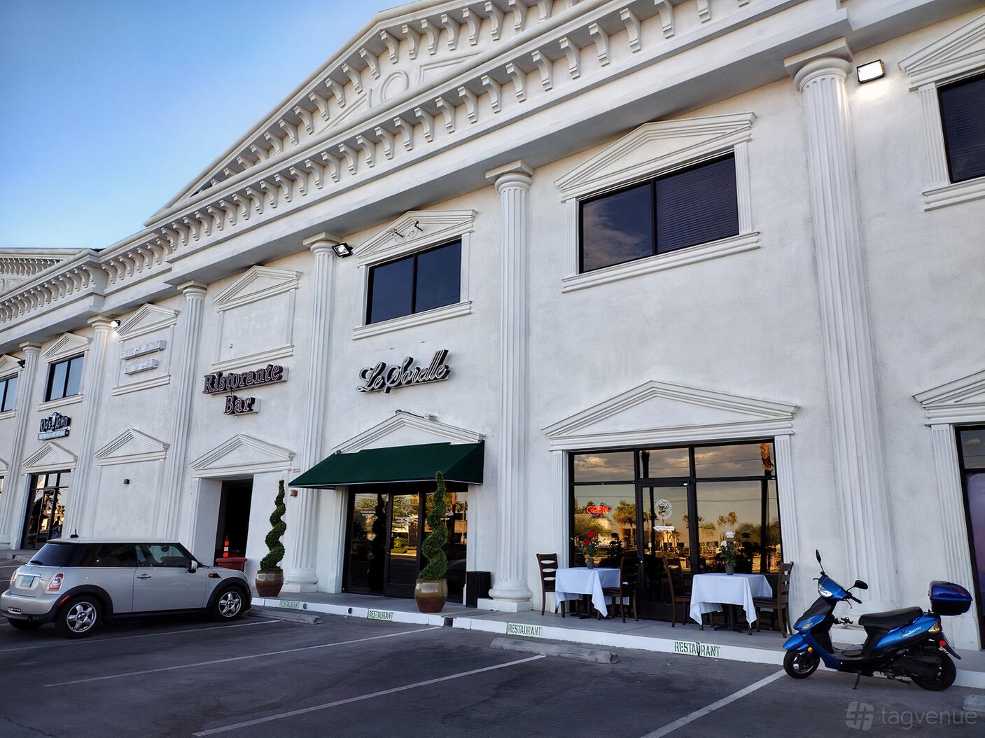 A restaurant with a grand white facade, large arched windows, and an awning at LE SORELLE RESTAURANT AND BAR.