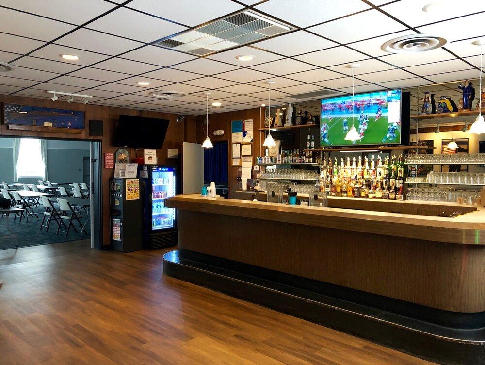 A community centre with a wooden bar, liquor shelves, and wall-mounted TV at The American Legion Post 1941.