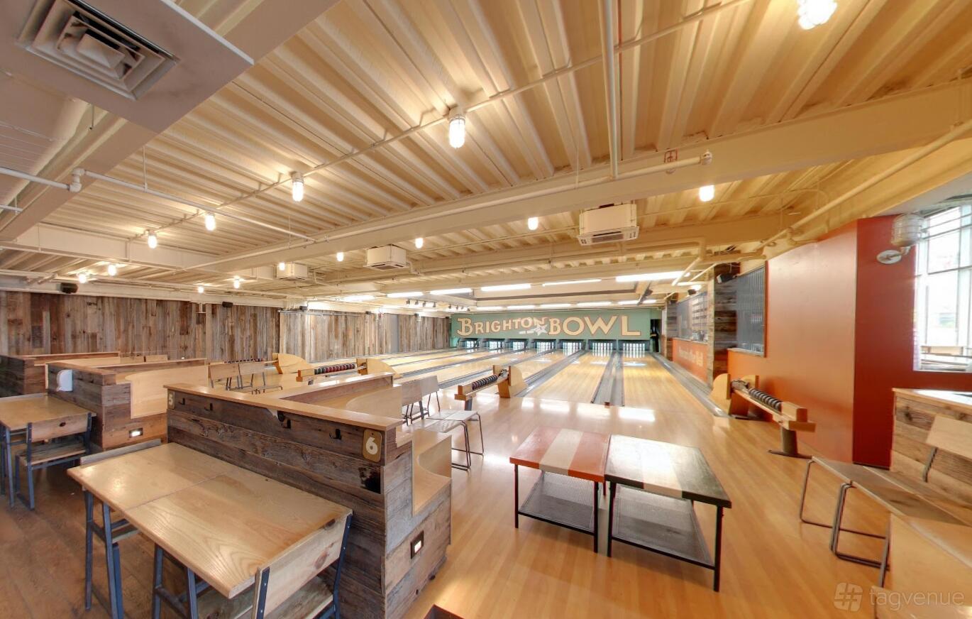 A bar with wooden tables, bench seating, and multiple bowling lanes at Brighton Bowl.