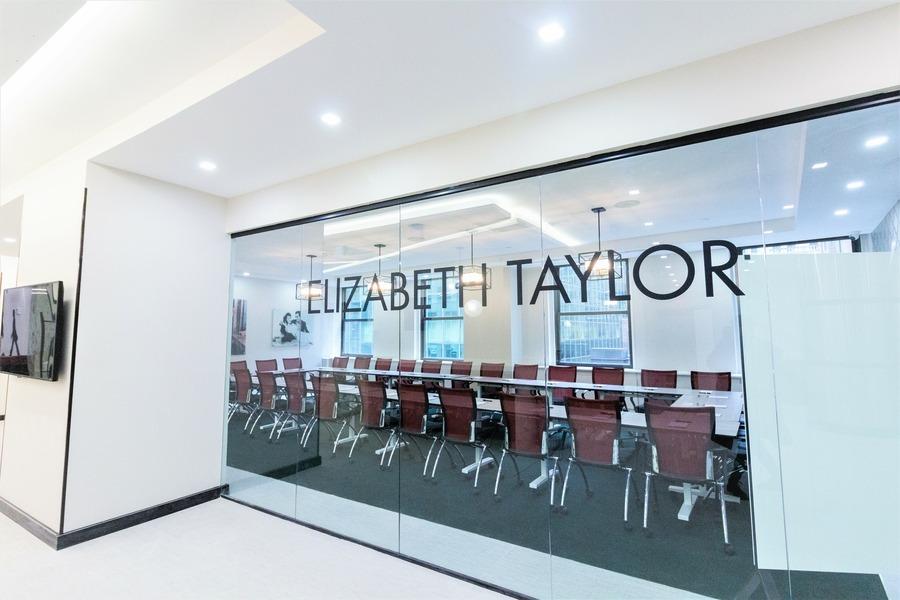 A meeting room with a long conference table, leather chairs, and glass walls at Midtown East Jay Suites.