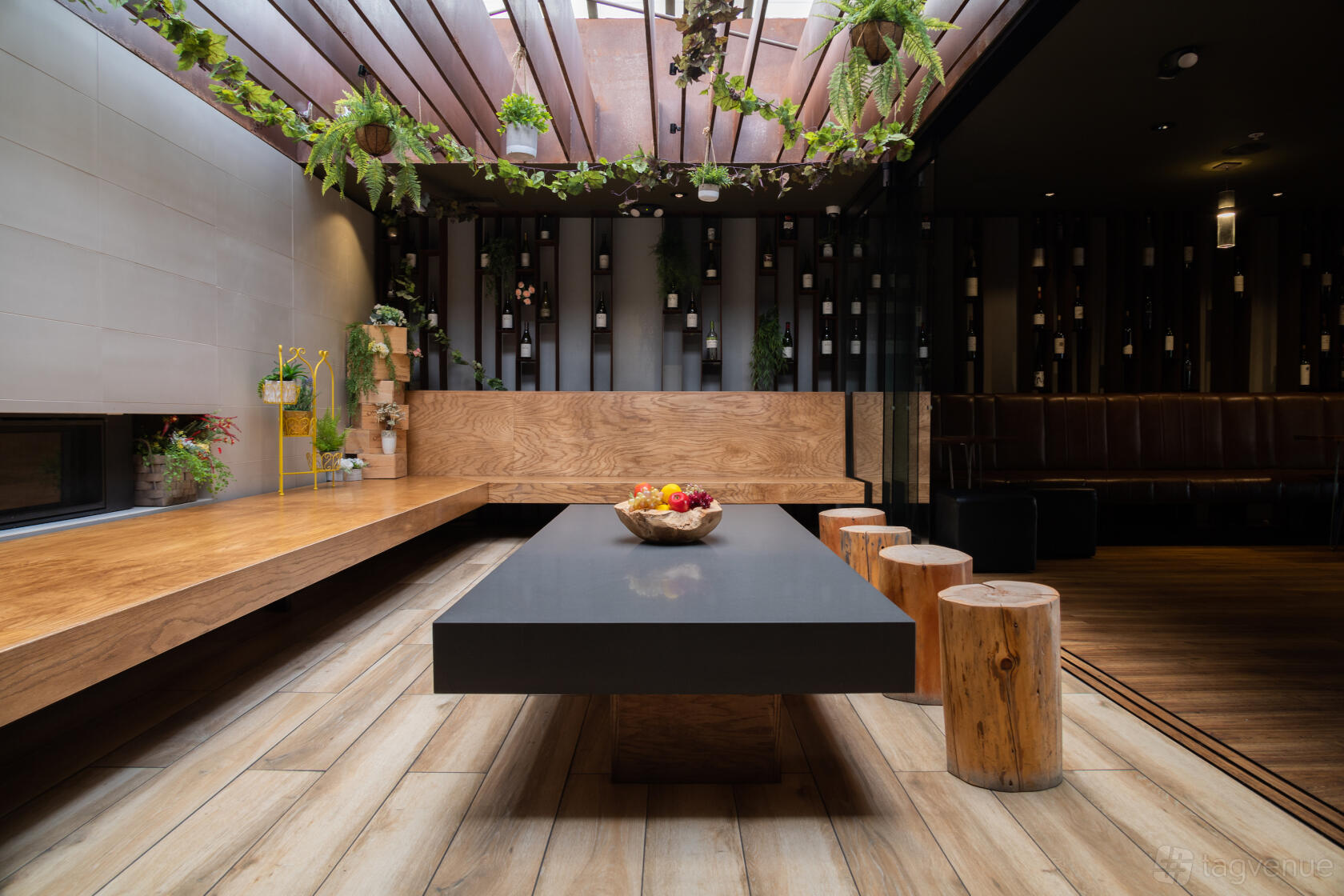 An event space in a bar with a skylight, hanging plants, wooden benches, and a sleek black table at Sippin'.
