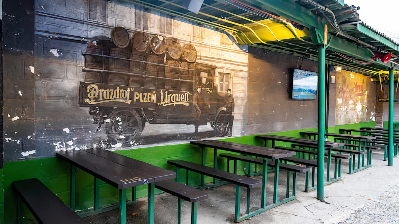 An outdoor beer garden with long wooden picnic tables, a mural, and a covered awning at Bohemian Hall and Beer Garden.