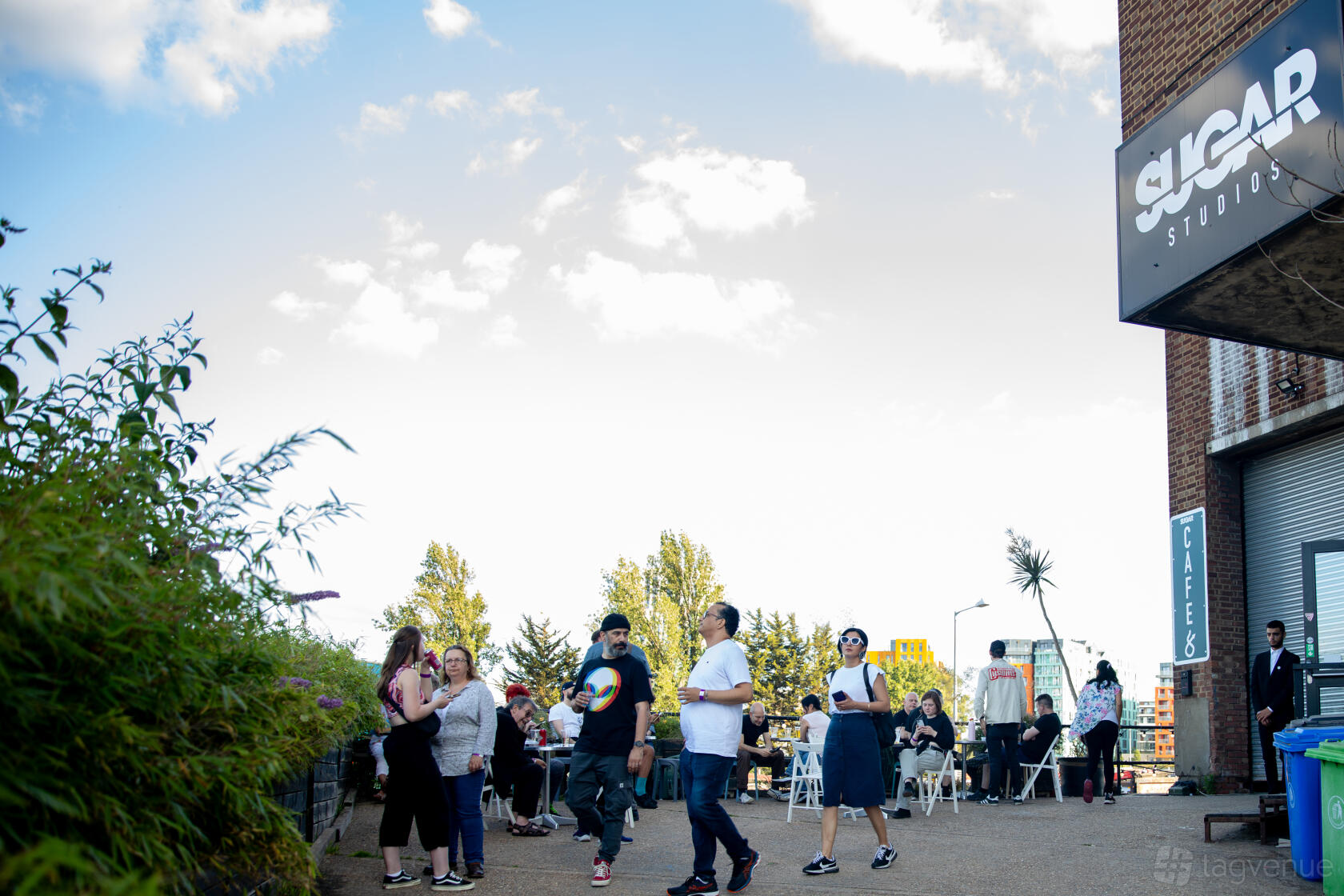 An outdoor area at a film and photo studio with people gathered near the entrance and seating at Sugar Studio.