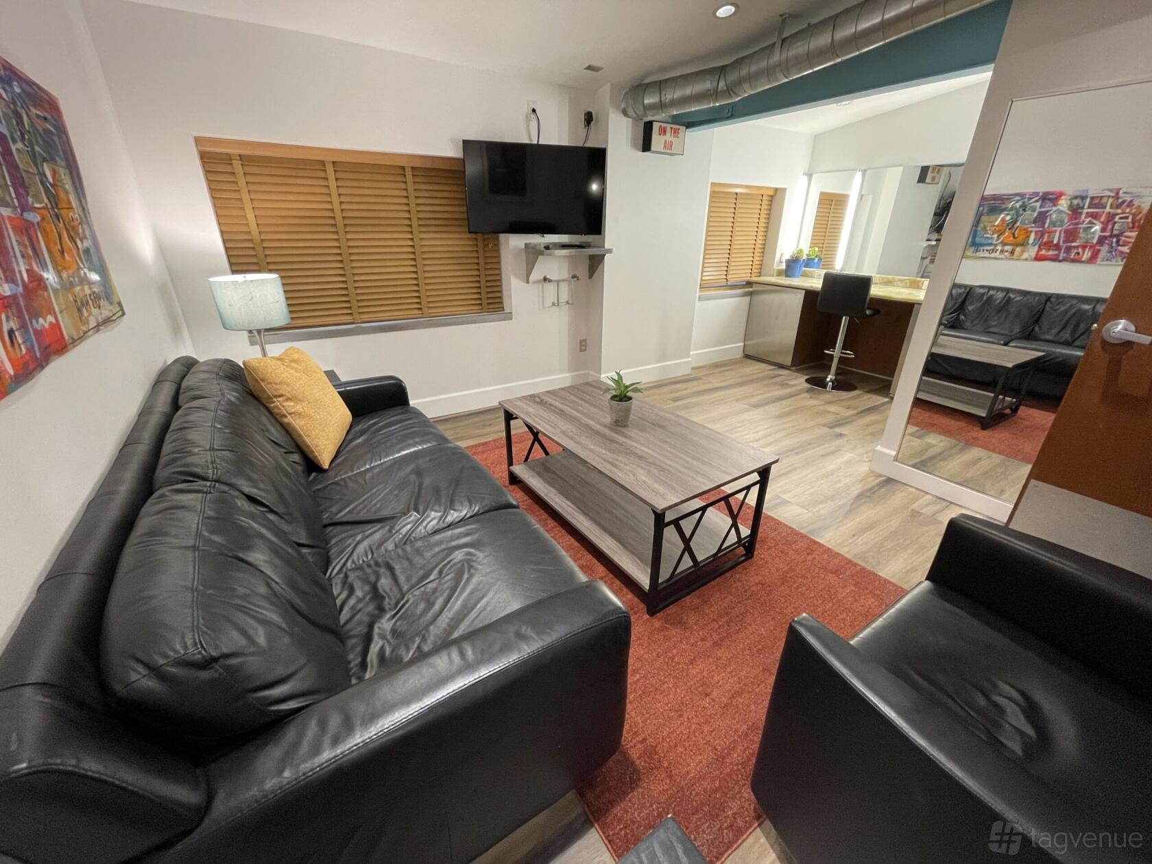 A photo studio lounge with a black leather sofa, armchair, coffee table, and wall-mounted TV at BLT STUDIOS.