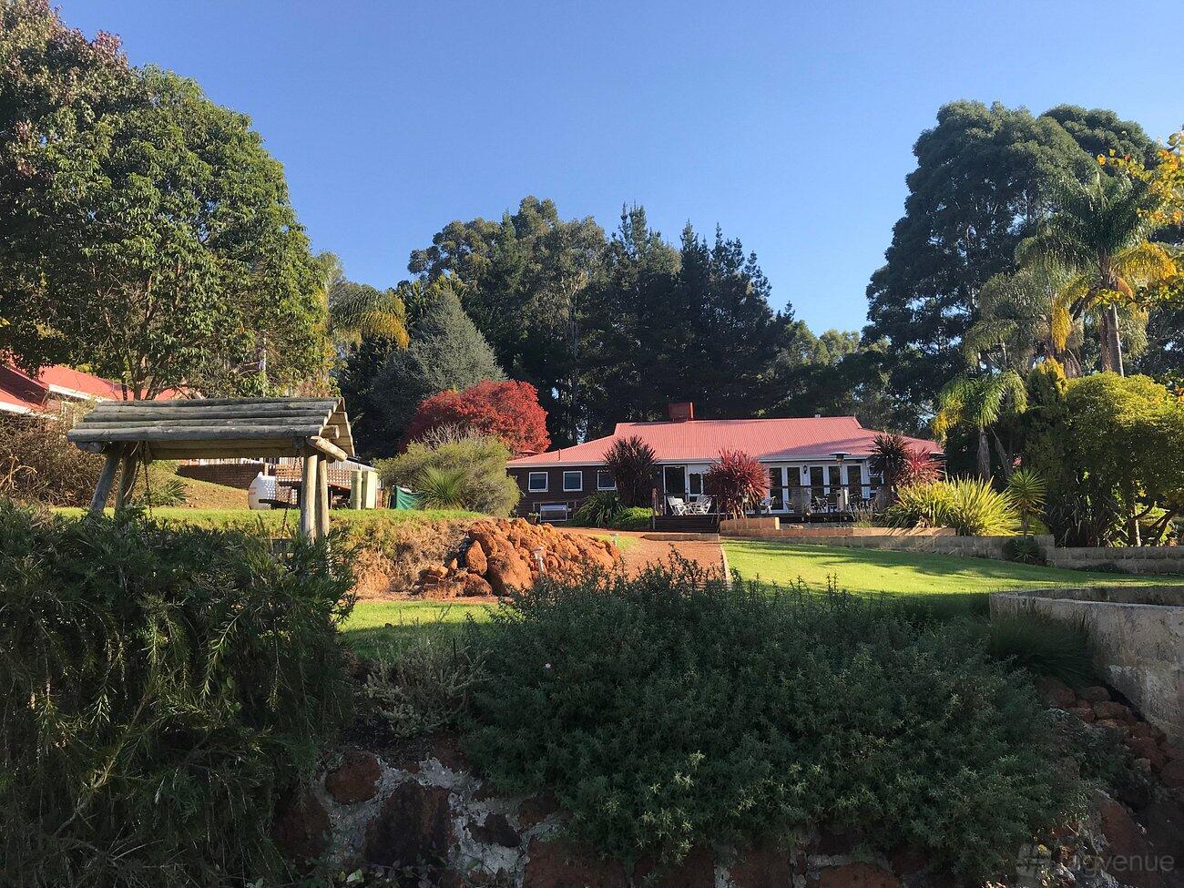 A hotel with a red-roofed building surrounded by landscaped gardens, tall trees, and a wooden swing at Forest Lodge Resort.