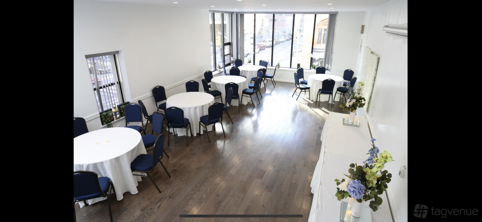 A loft venue with large windows, round tables with white linens, and hardwood floors at Hidden City.