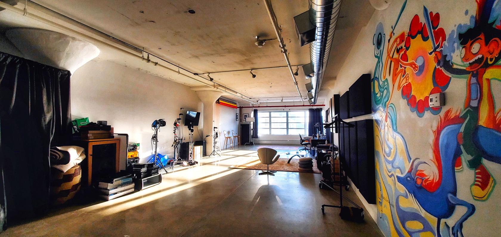 A photo studio with large windows, exposed ceiling pipes, colorful wall mural, and studio lighting at Indigo Soul NYC.