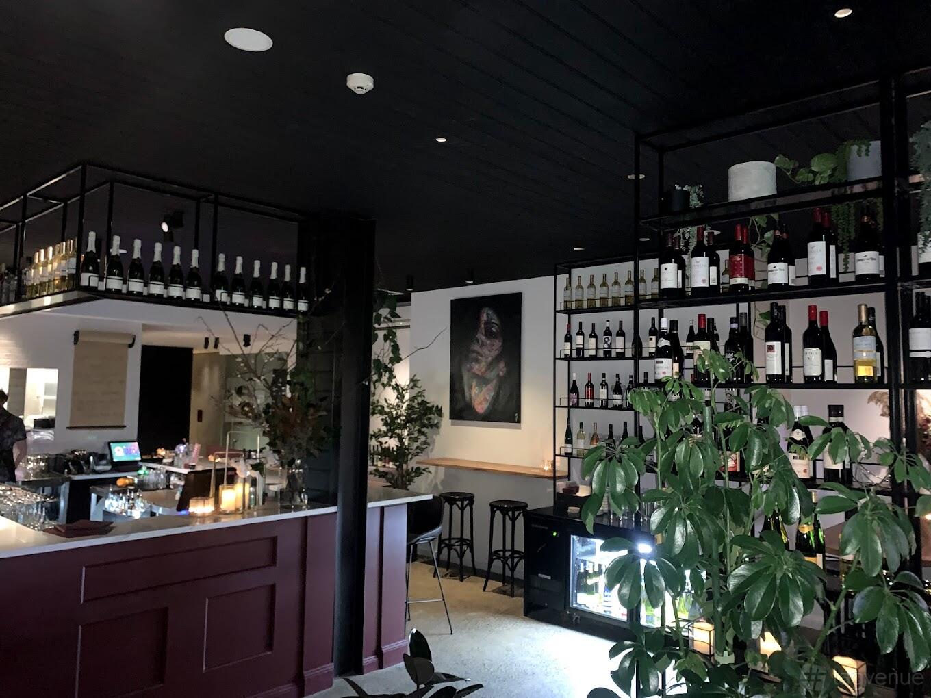 A restaurant with a wine display wall, candlelit bar, and indoor plants at Attria Wine Bar.