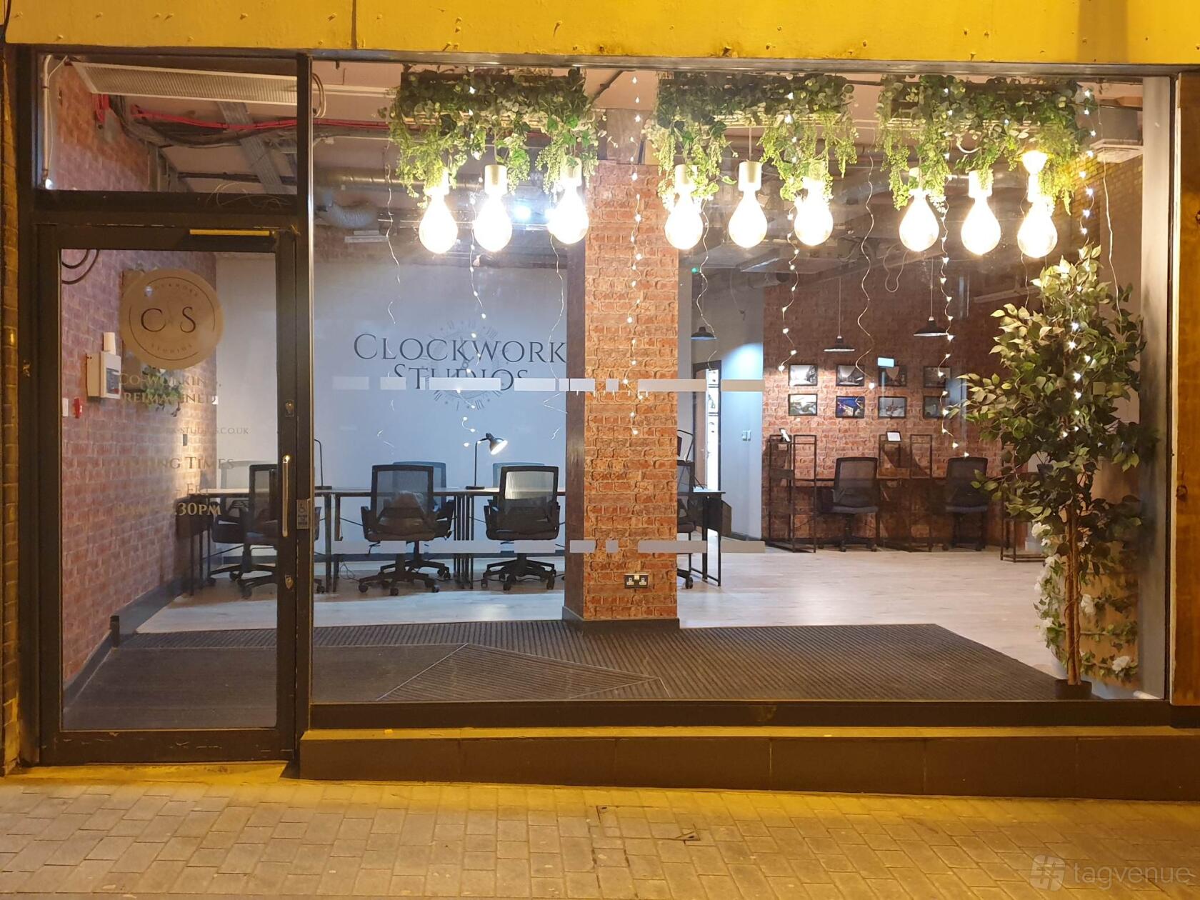 A coworking space with exposed brick walls, hanging light bulbs, and workstation desks at Clockwork Studios CIC.