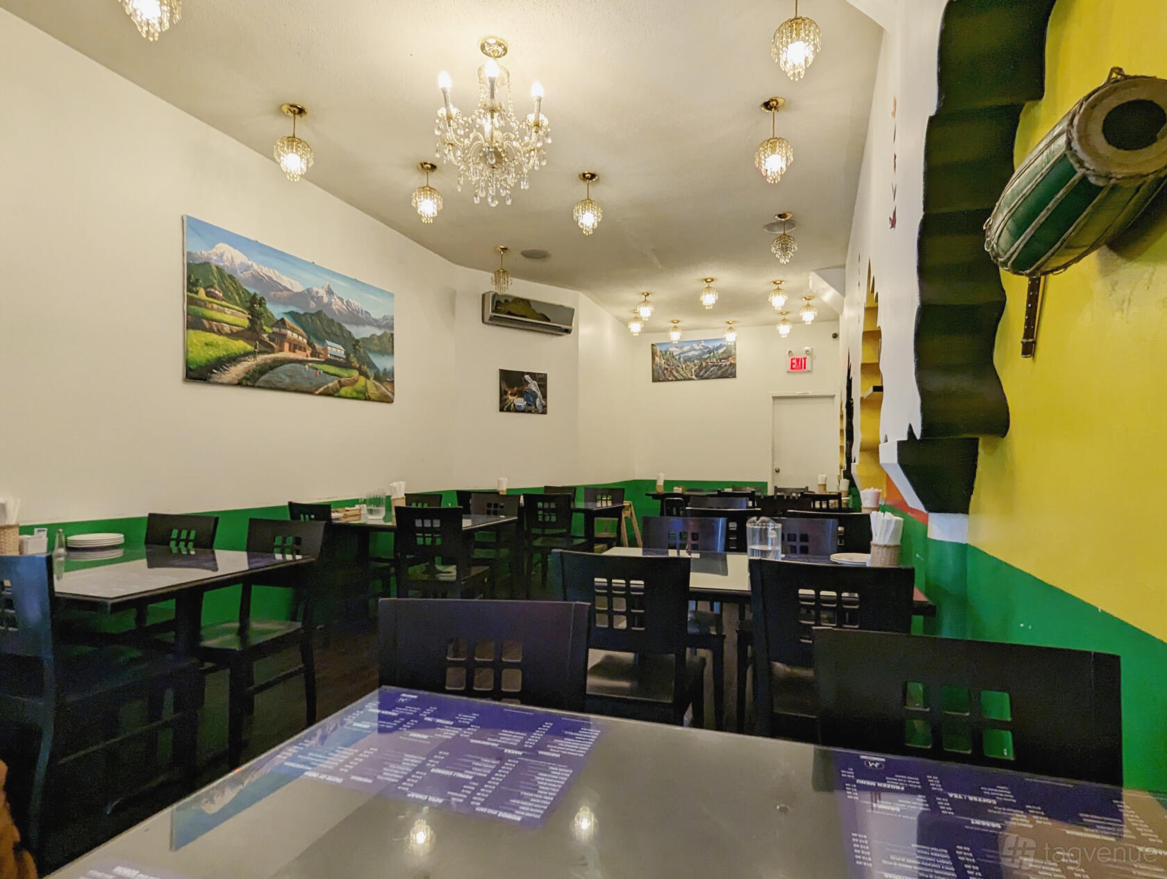 A restaurant dining room with black tables and chairs, chandeliers, wall art, and green-and-yellow accents at Momozone.