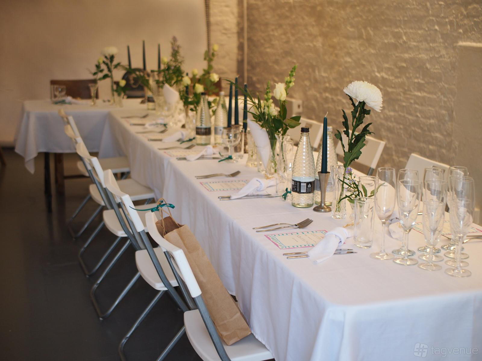 An art studio with white brick walls, long tables draped in white linens, floral centerpieces, and rows of chairs at Green Lens Studios - NORTH4.