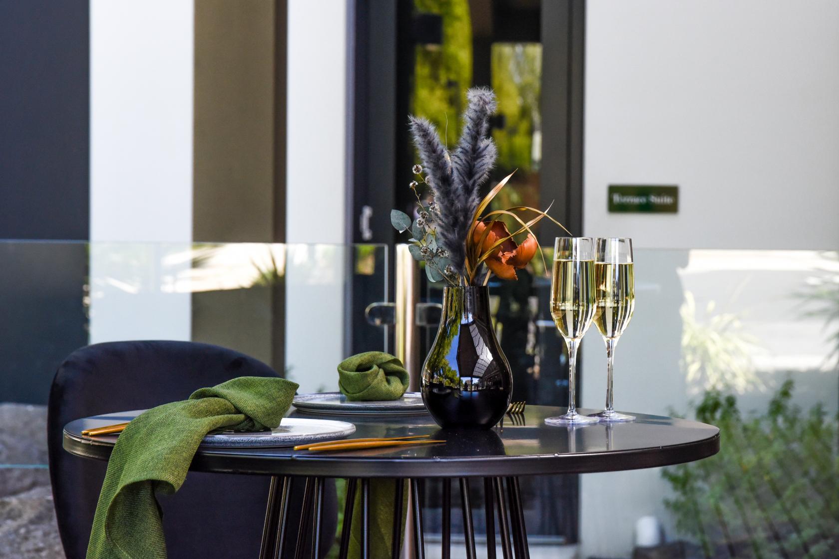 A hotel terrace with a round table set for two, green napkins, and champagne glasses at The Terrace Hotel.