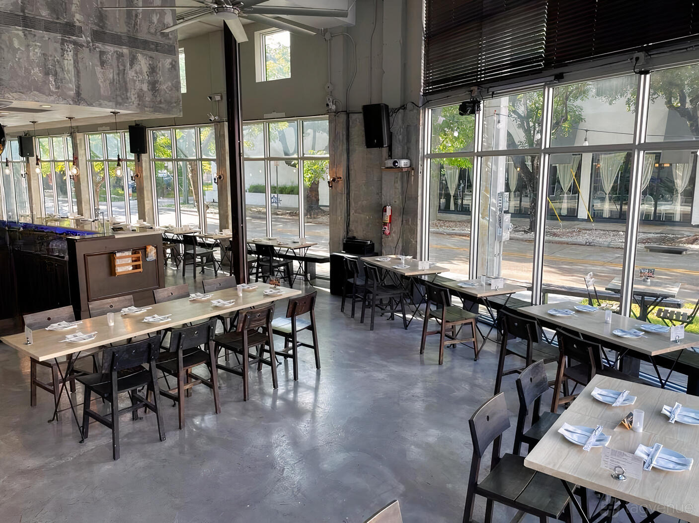 A restaurant with floor-to-ceiling windows, concrete floors, and neatly set tables at Daek Thai Eatery.