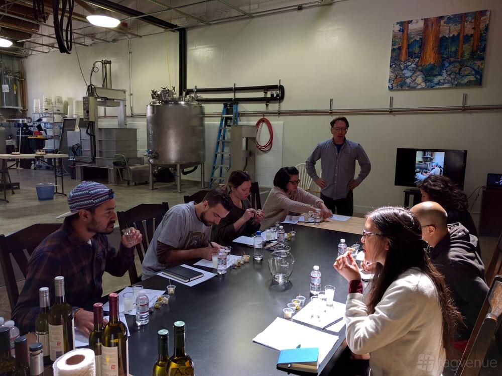 An event space in a bar with a long table, sake tasting setup, and brewing tanks in the background at Sequoia Sake.