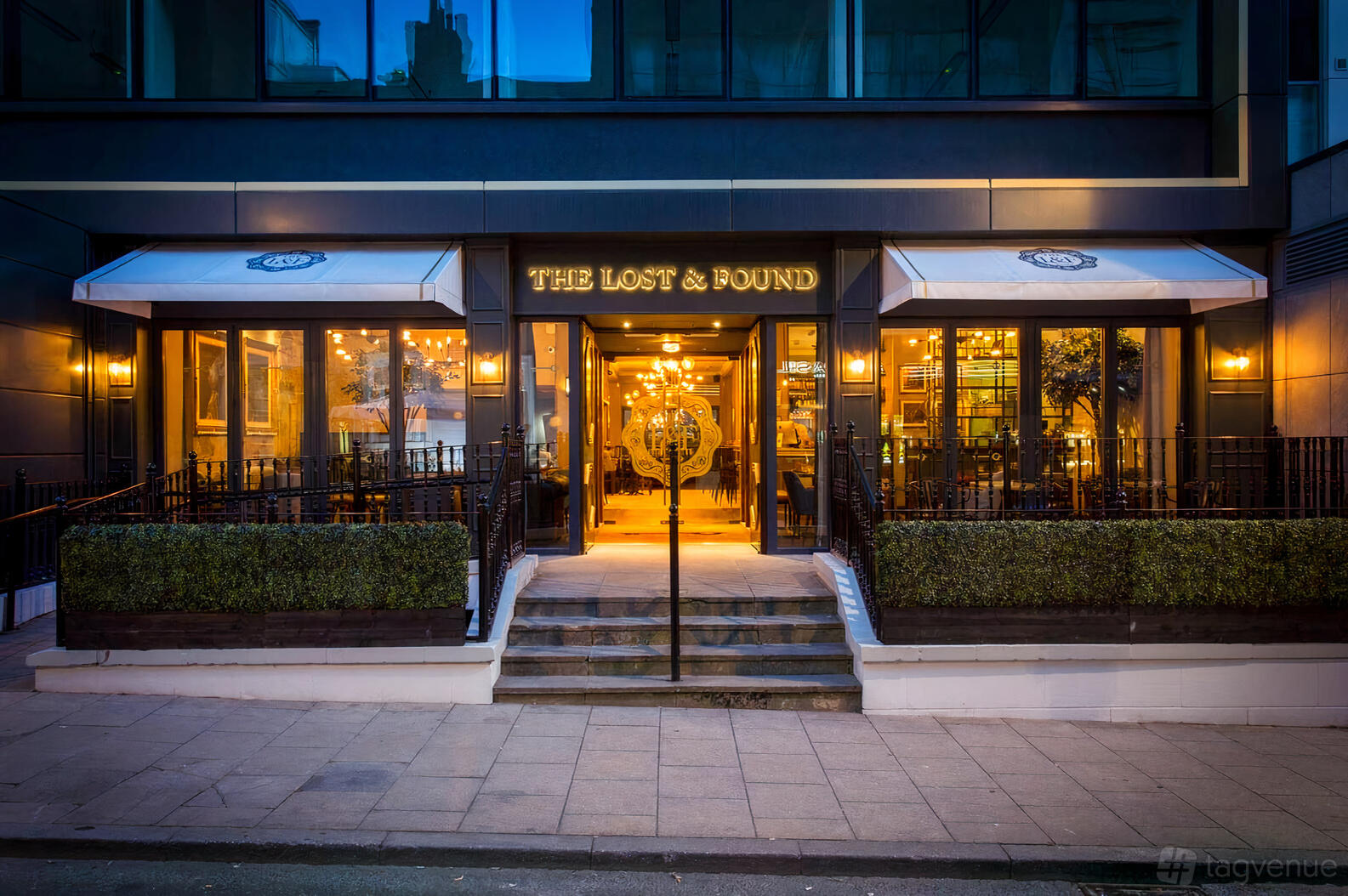 A pub entrance with large windows, outdoor seating, and warm lighting at The Lost and Found Greek Street.