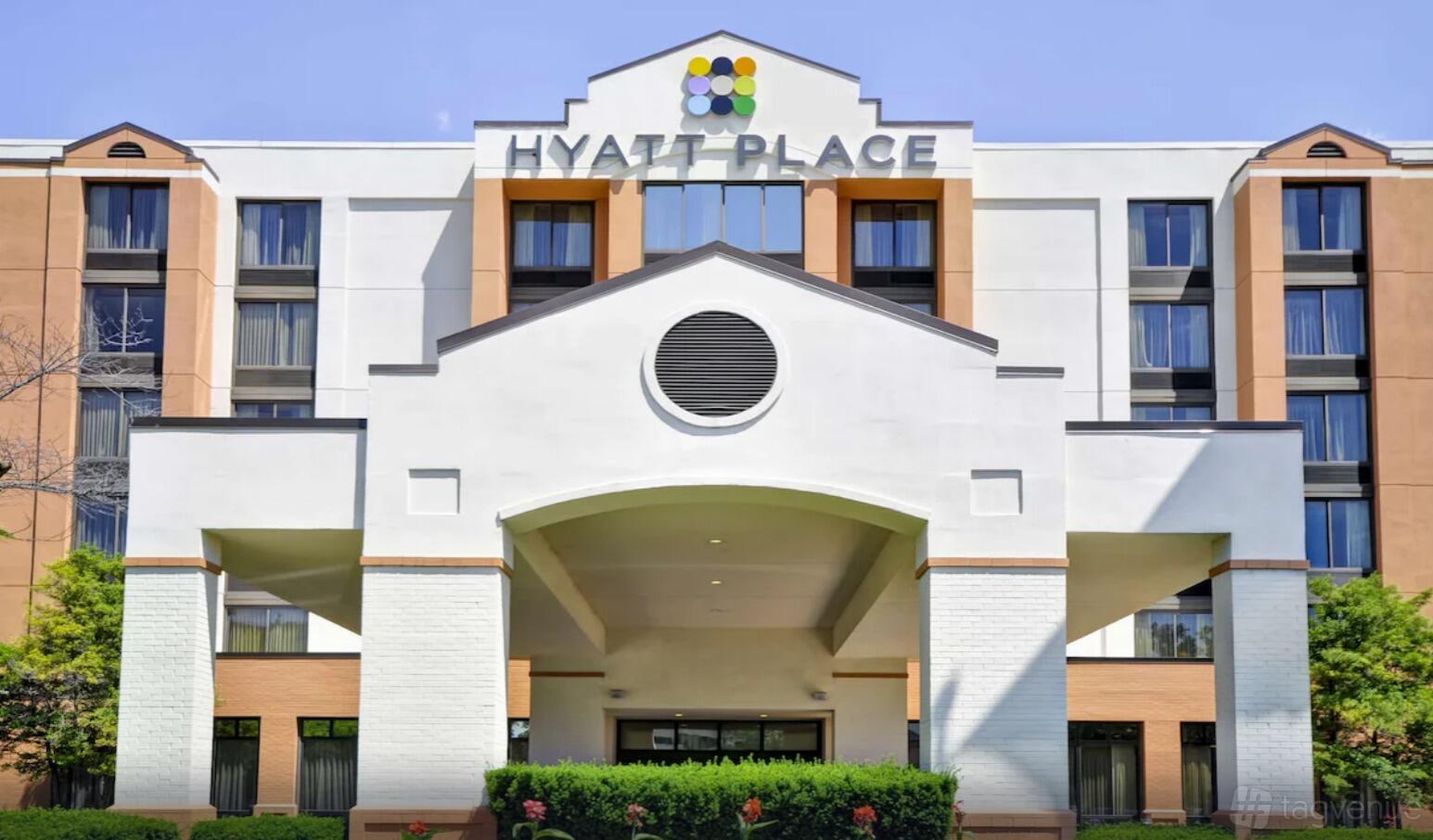 A hotel with a white entrance façade, large circular vent, and landscaped bushes at Hyatt Place Dallas North Galleria.