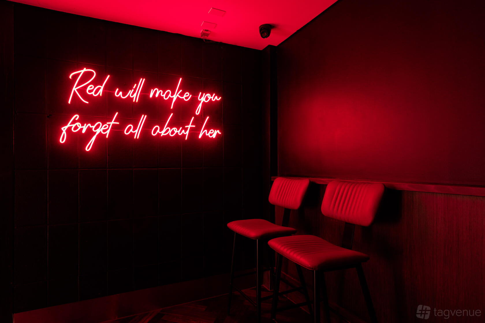 A cocktail bar corner with red neon signage, black tiled walls, and red upholstered bar stools at Little Red's Cocktail Bar.