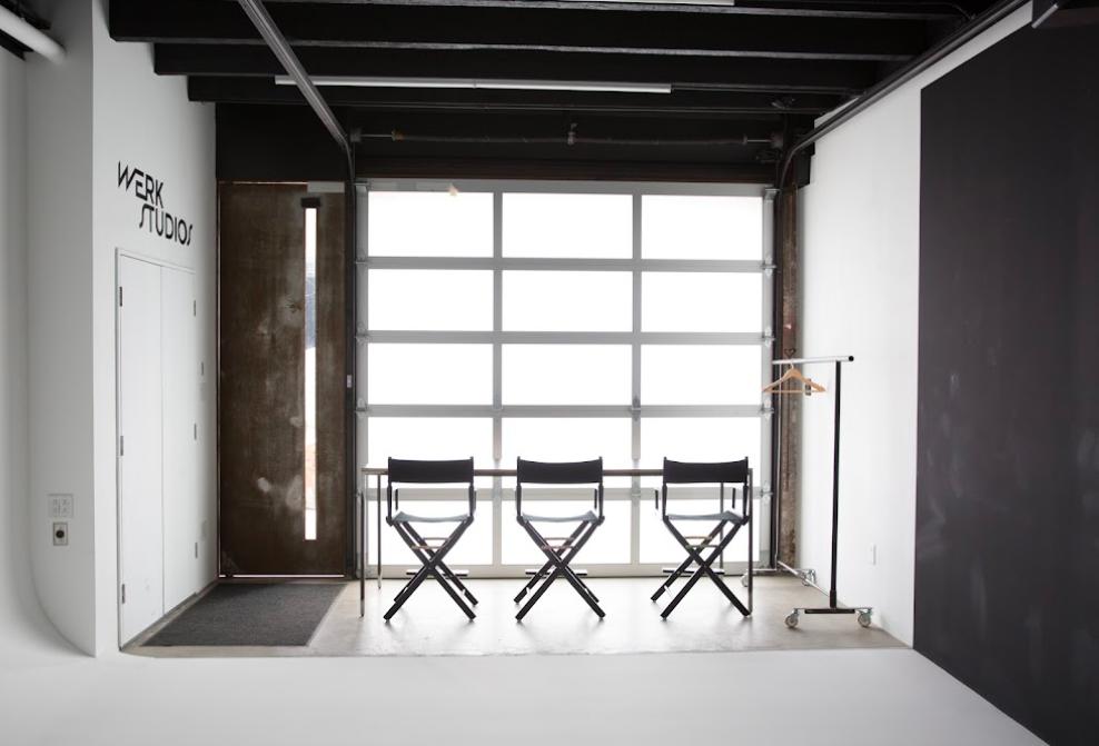A photo studio with director chairs, a white cyclorama wall, and a large frosted glass garage door at Werk Studios.