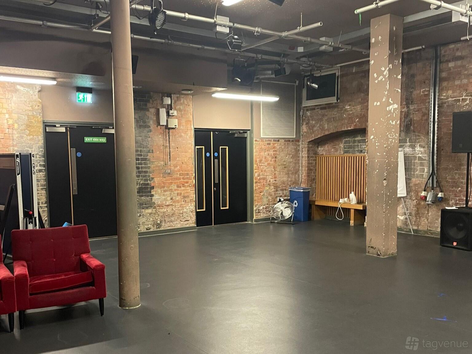 An event space with exposed brick walls, concrete pillars, and stage lighting at Collective Acting Studio.