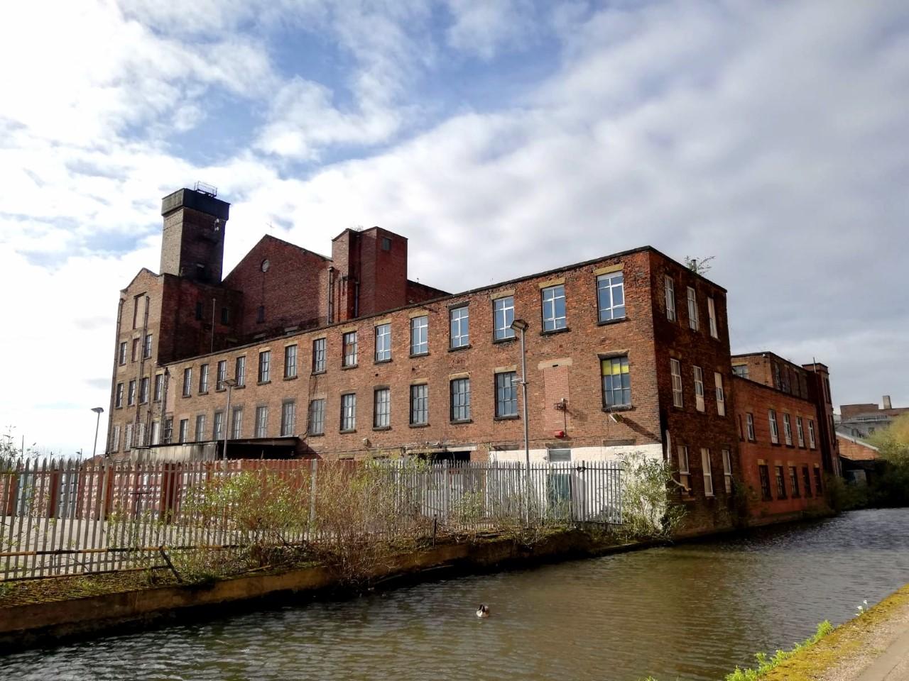 A brick industrial building with large windows beside a canal at Wellington Studios.