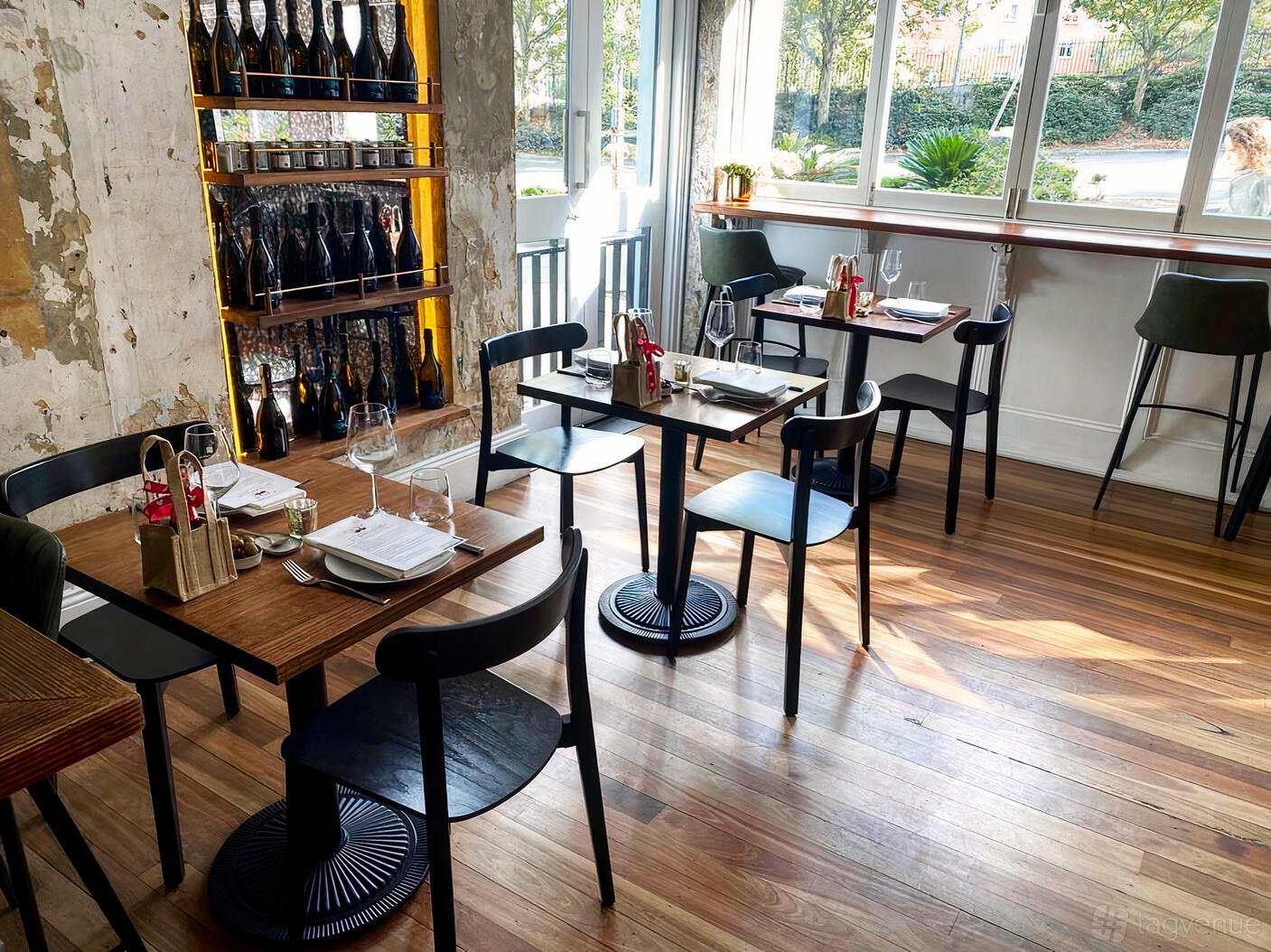 A restaurant with wooden floors, small square tables, black chairs, and a wine display at Figo Ristorante & Bar.