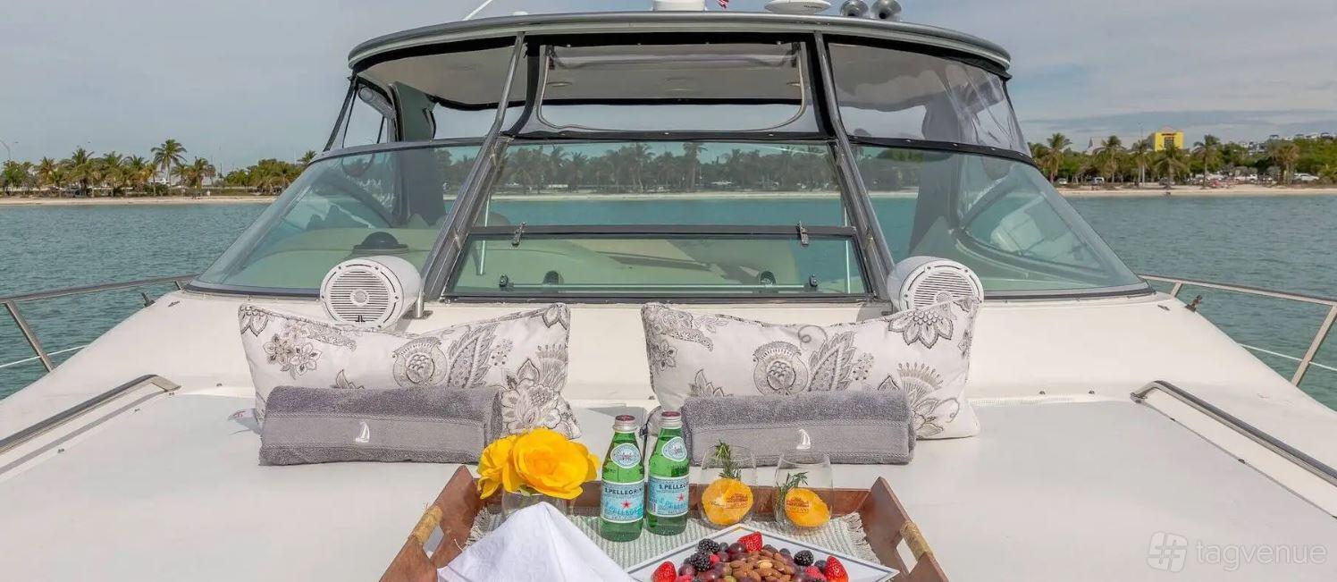 A boat deck with patterned pillows, towels, and a tray of sparkling water, fruit, and desserts at Beeyond Boats - Harbor West Marina Miami.