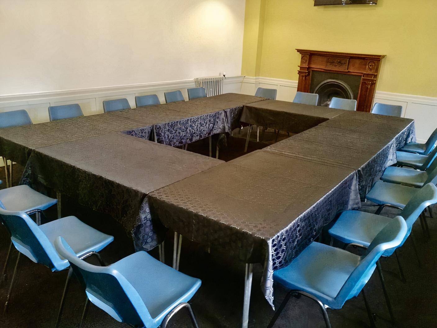 A meeting room with blue chairs around tables arranged in a U-shape and a decorative fireplace at Destiny Church Shawlands.