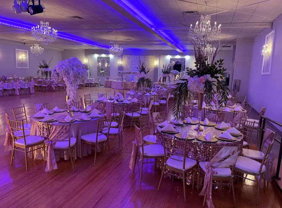 An event venue with gold chairs, round tables draped in sequined linens, and blue uplighting at Fountainblu Event Center.