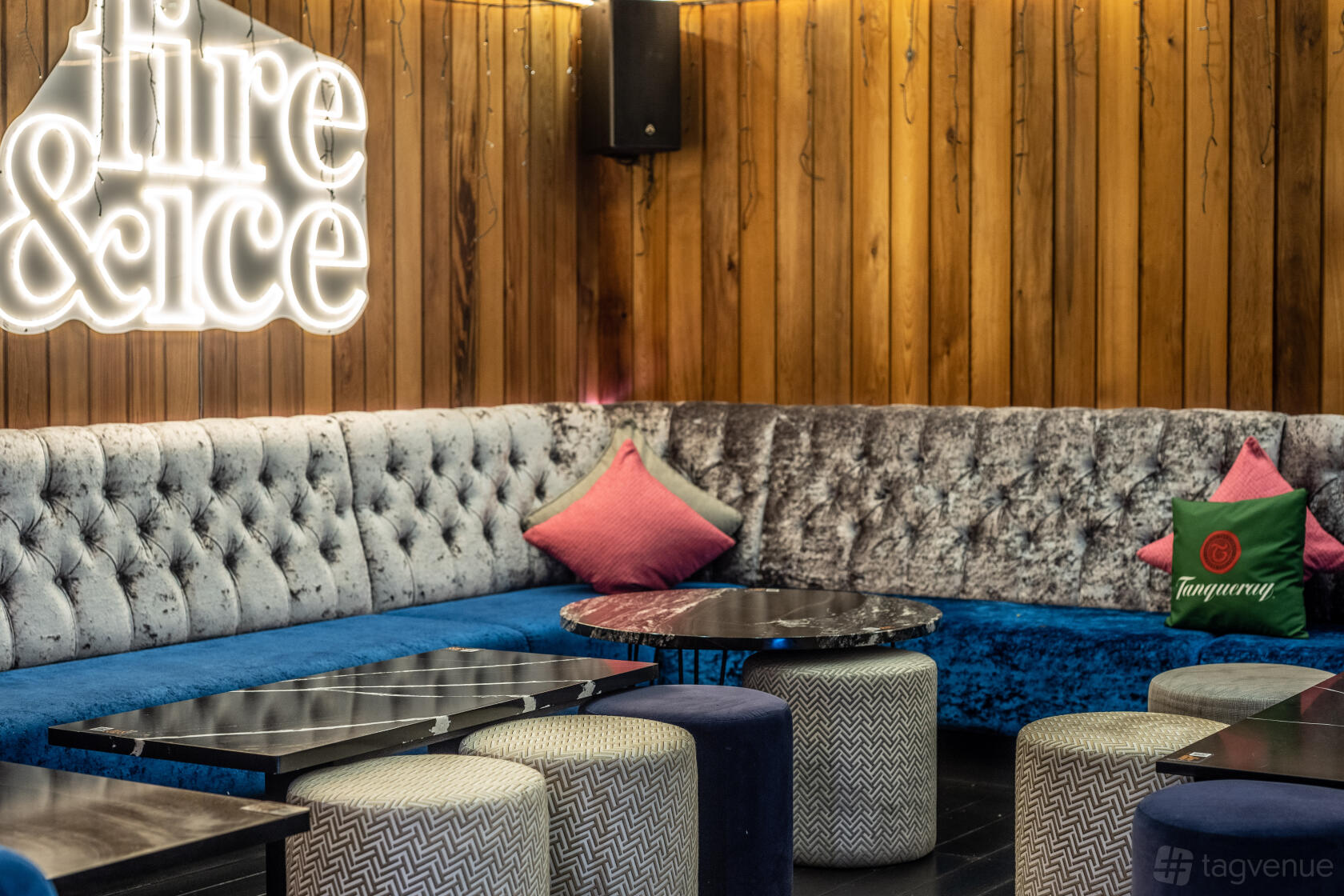 An outdoor lounge area with tufted velvet seating, wood panel walls, round tables, and accent pillows at Fire & Ice Lounge Bar.