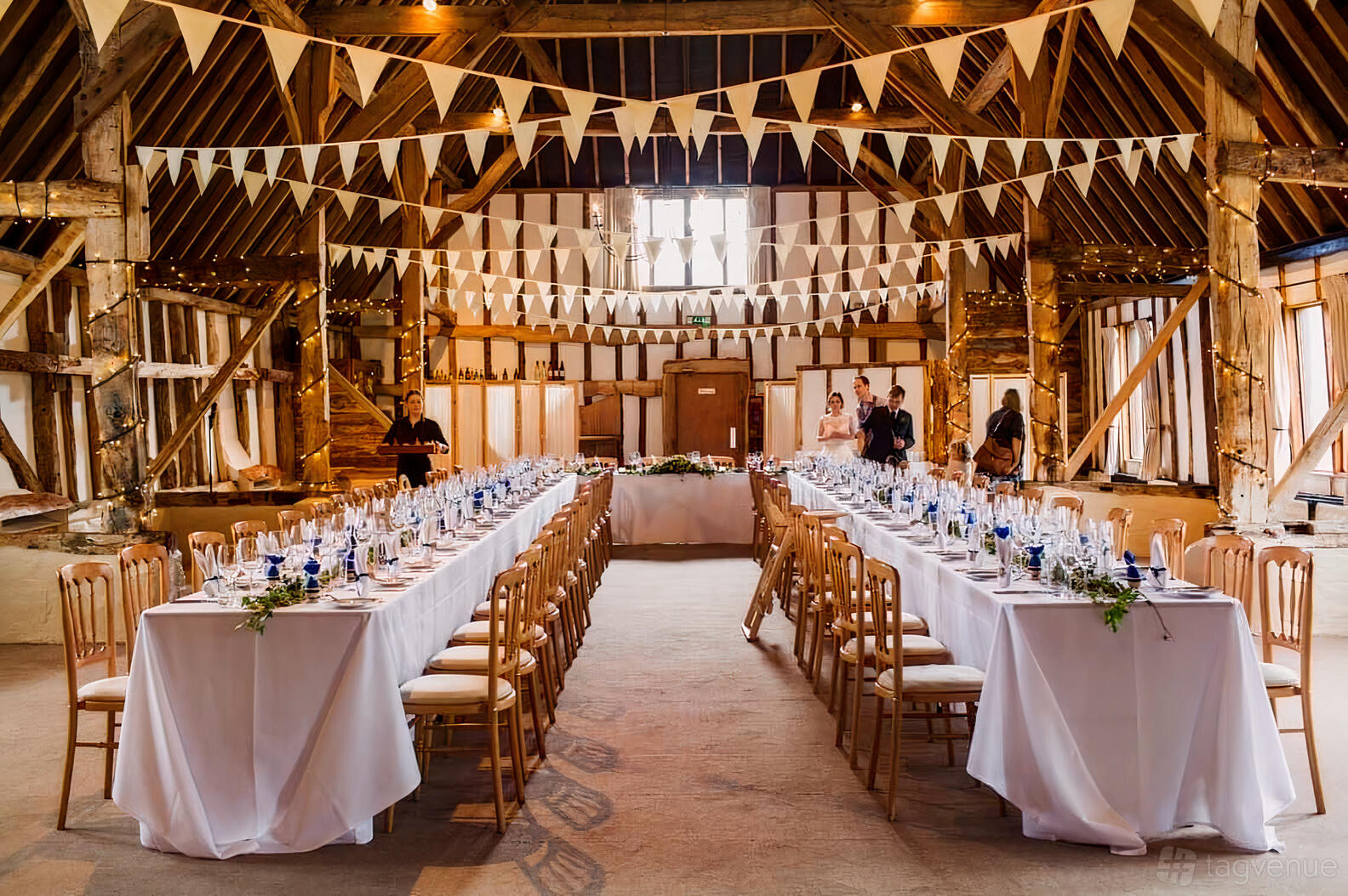 A rustic barn with exposed beams, bunting decorations, and long banquet tables with white linens at Clock Barn.
