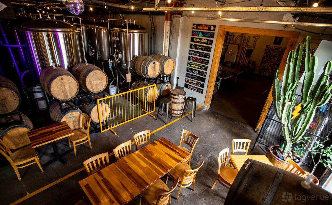 An event space in a brewery with stainless steel tanks, stacked barrels, and long wooden tables at Diebolt Brewing Company.