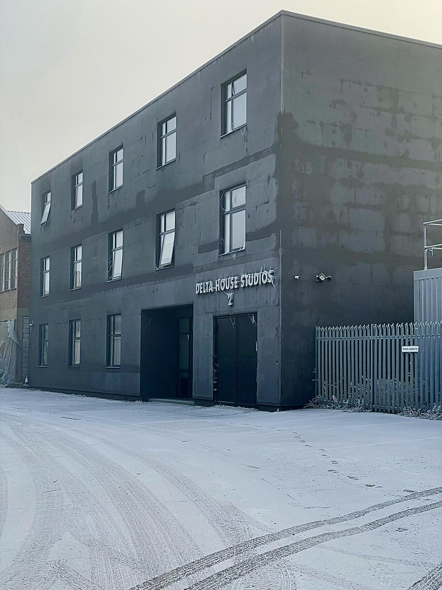 A grey industrial film and photo studio exterior with large windows and metal fencing at Delta House Studio.