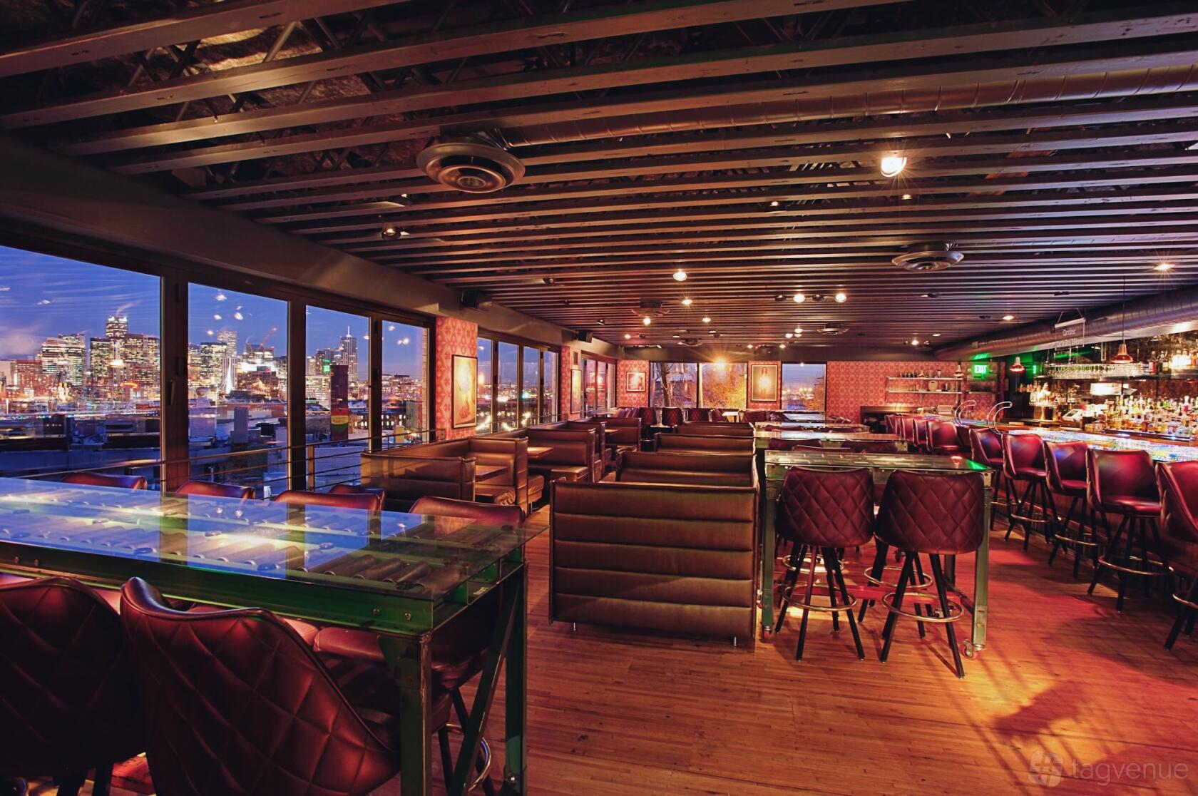 A lounge with leather booth seating, city skyline views through large windows, and a backlit bar at Linger.