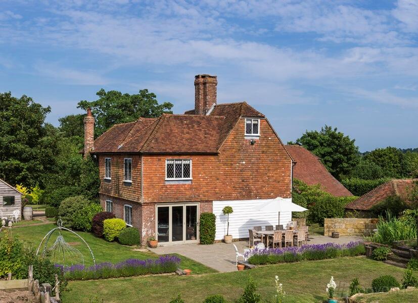 A country house with red brick exterior, leaded windows, garden patio, and outdoor dining at Fair Oak Farm.