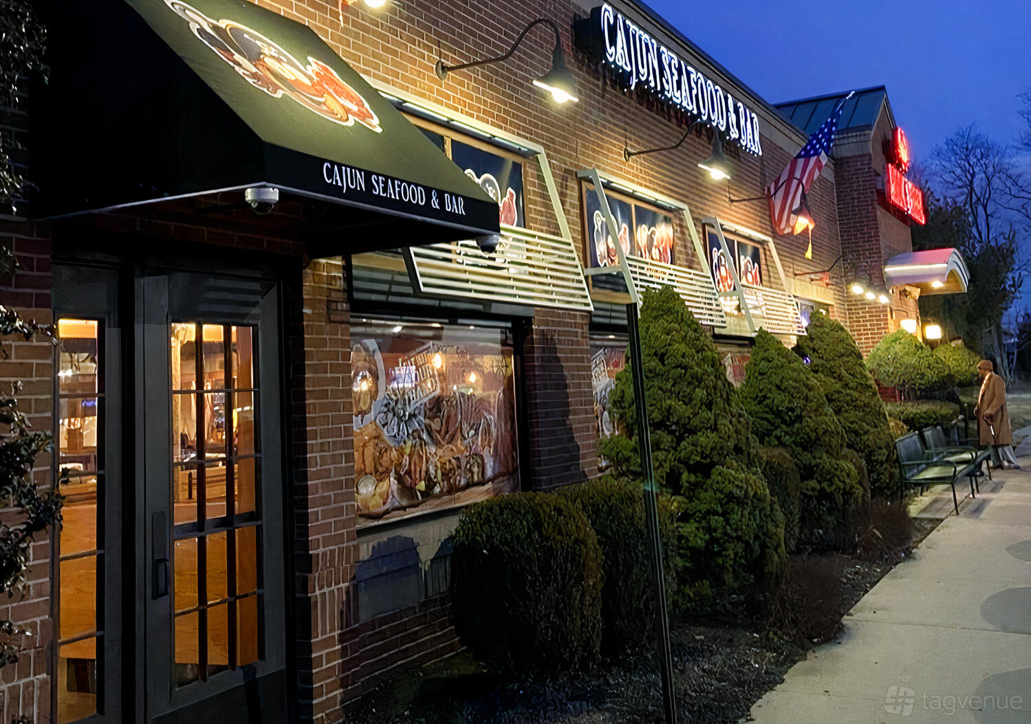 A restaurant with brick exterior, illuminated signage, window awnings, and trimmed bushes at Hook & Reel- Union.