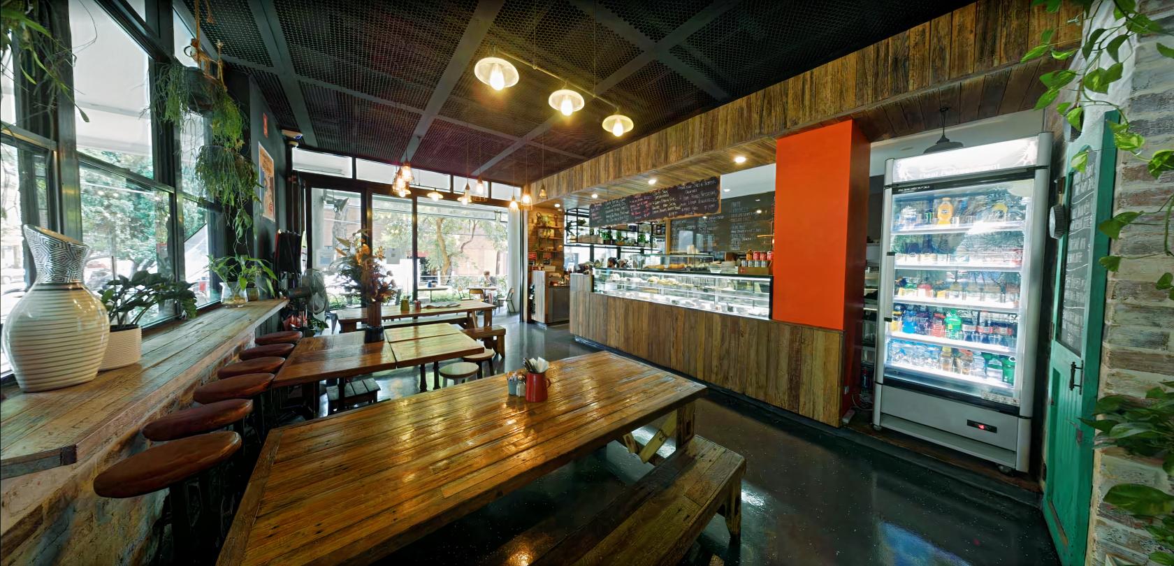 A cafe with wooden communal tables, chalkboard menu, and floor-to-ceiling windows at Eggspresso.