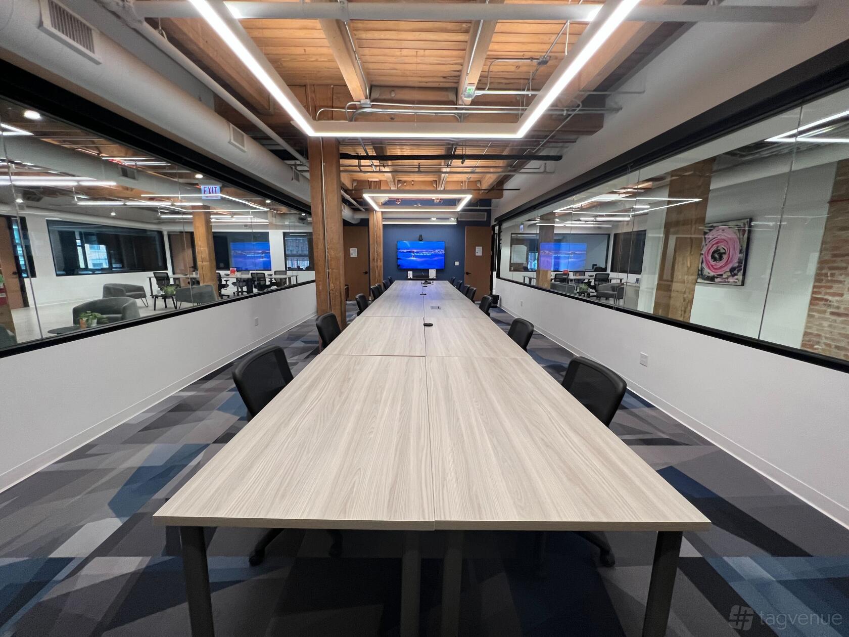 A training room with a long conference table, ergonomic chairs, and exposed wood ceilings at Workbox - River North.