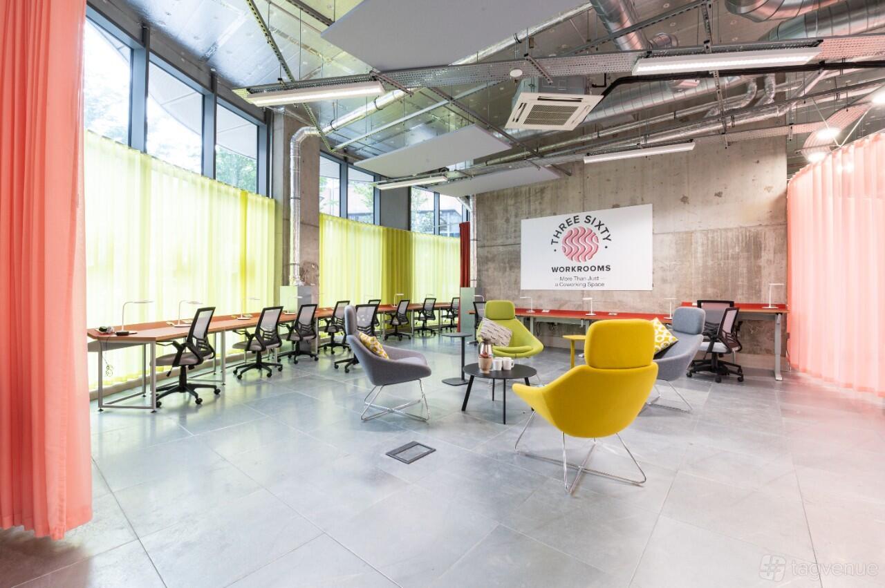 A coworking meeting room with floor-to-ceiling windows, concrete walls, and colorful chairs at Three Sixty Workrooms.