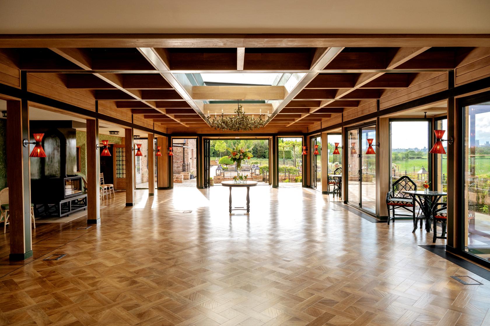 An event space with parquet wood floors, glass walls, red wall sconces, and countryside views at The Old Hall Ely.