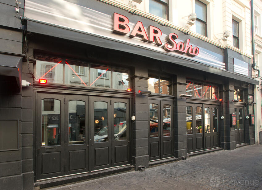 A pub with a black facade, large street-facing windows, and the Bar Soho sign above the entrance at Bar Soho.