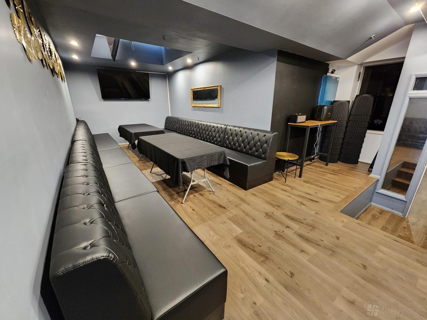 An event space in a loft with black tufted leather banquettes, wood flooring, and large TV at Loft on George.
