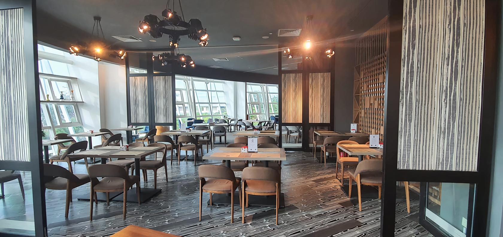 An event space in a restaurant with wooden tables, cushioned chairs, and floor-to-ceiling windows at PEN & INC, NTU.