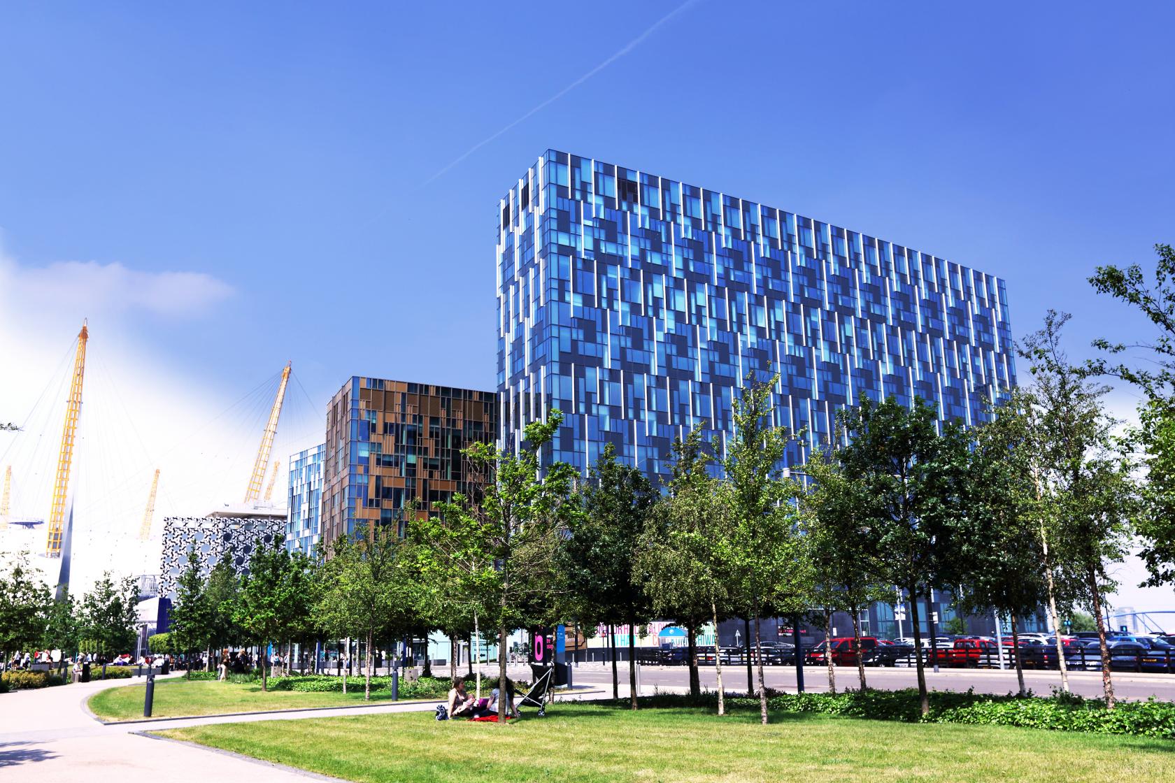 A contemporary meeting centre with a blue geometric glass facade and surrounding trees at Landmark: North Greenwich, London.