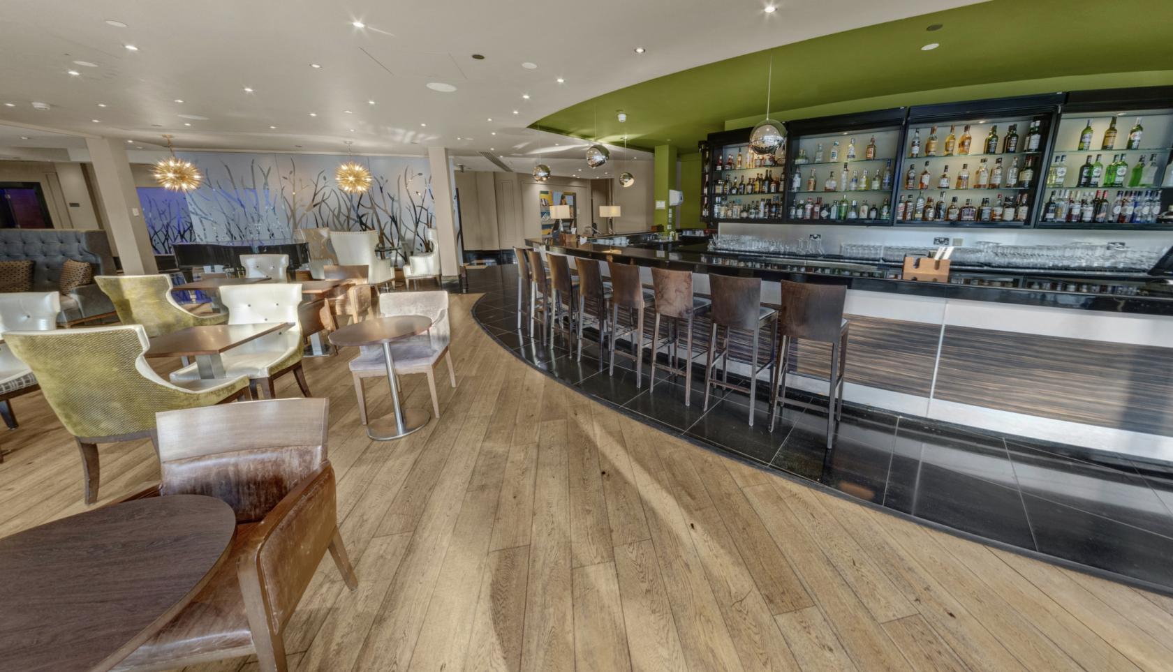 A hotel terrace bar with a curved wood floor, a long counter with high chairs, and contemporary decor at Chelsea Harbour Hotel & Spa.