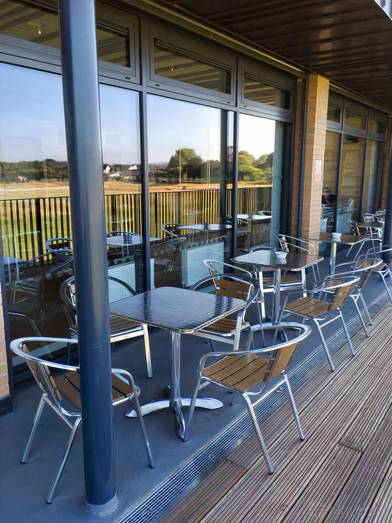 An outdoor lounge area with metal tables and chairs beside glass windows at Shaftesbury Park.