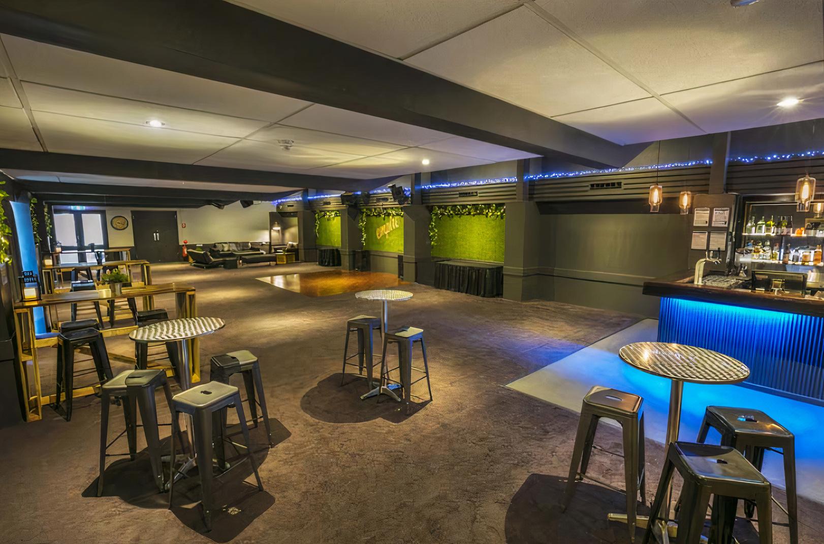 A hotel event room with metallic tables, bar stools, wall greenery, and accent lighting at Manhattan Hotel.