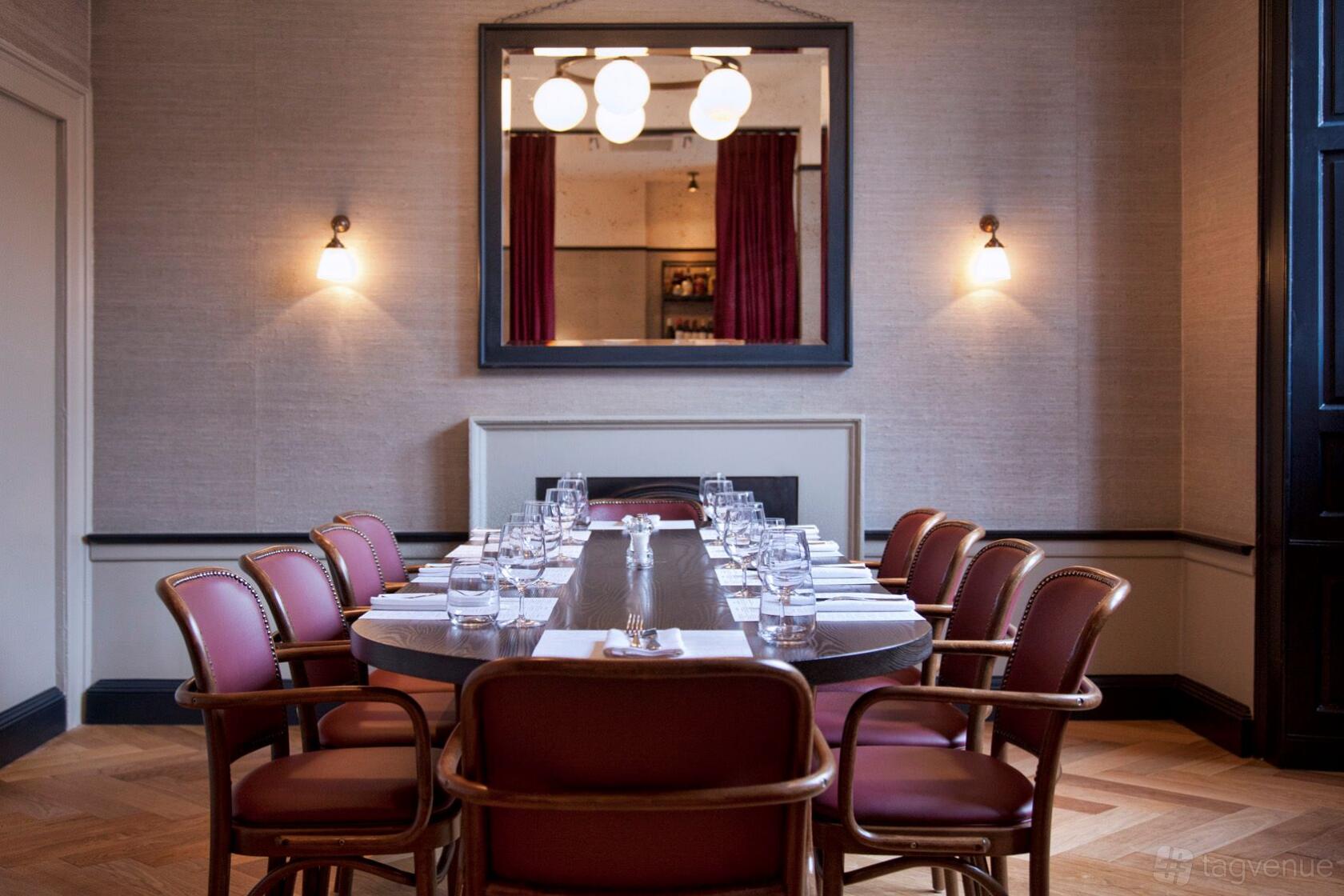 A dining room with a long oval table, red upholstered chairs, and wall sconces beneath a large mirror at Côte Brasserie Edinburgh.