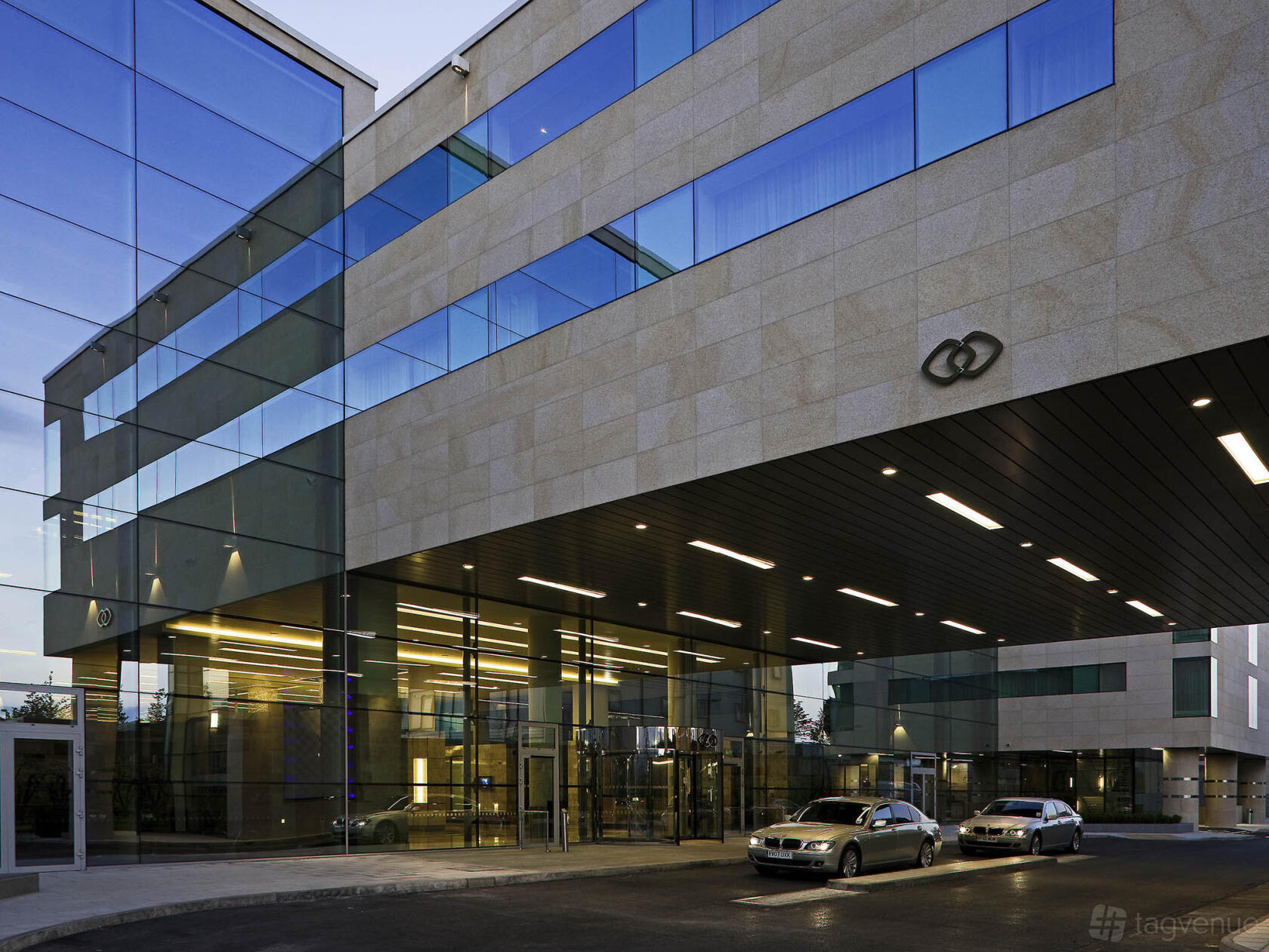 A hotel entrance with a glass facade, covered driveway, and parked cars at Sofitel London Heathrow.