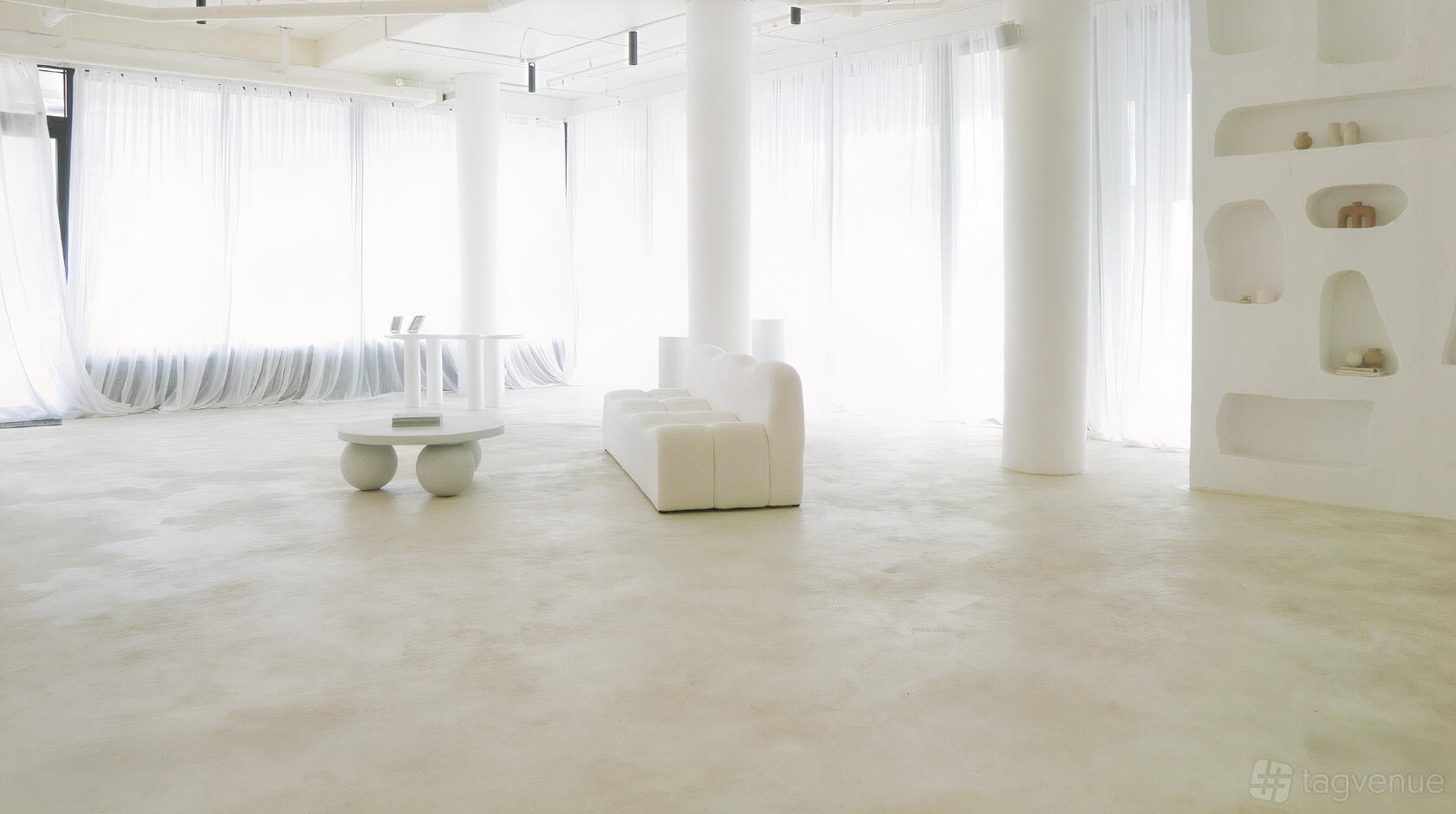 A photo studio with white floors, curved sofas, and sheer curtains at No Filter Studios.