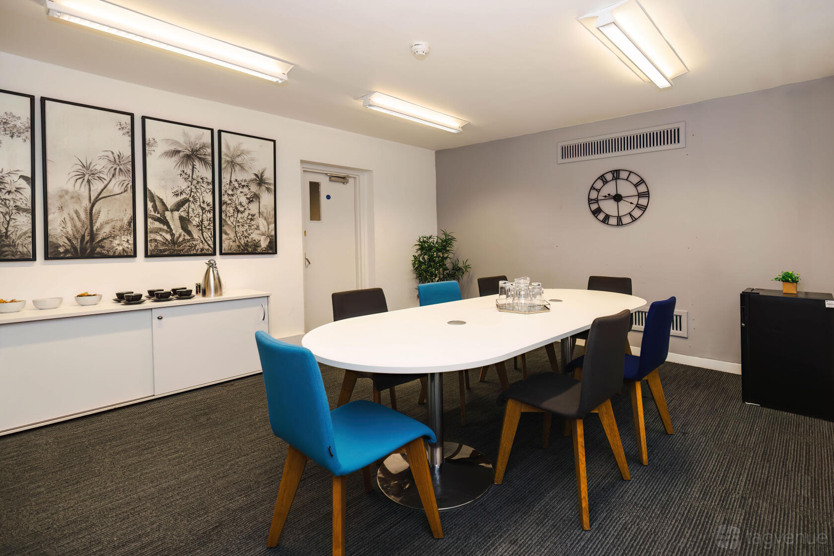 A meeting room with an oval table, mixed-color chairs, wall art, and a clock at Guy's and St Thomas' Hospital.